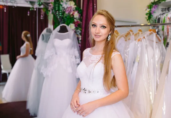 Femme essayant sur robe de mariée dans un magasin avec des femmes assistant . Photo De Stock