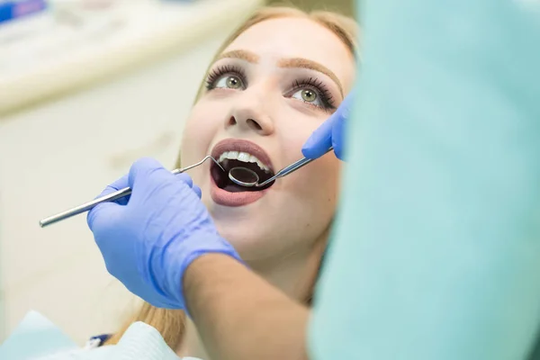 Närbild av ung kvinna sitter i tandläkare stolen med öppnade munnen på tandläkare kontor samtidigt ha undersökning — Stockfoto