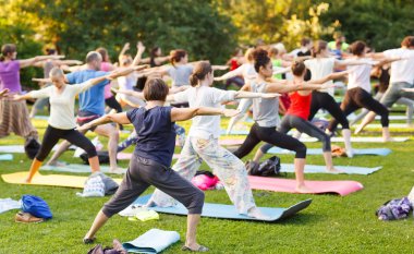 Büyük bir grup yetişkin parkta yoga dersine katılıyor.