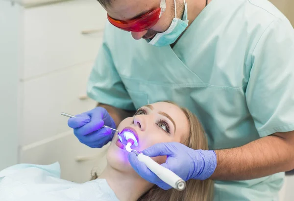 Dentista haciendo procedimiento con la luz UV de curado dental en la clínica — Foto de Stock