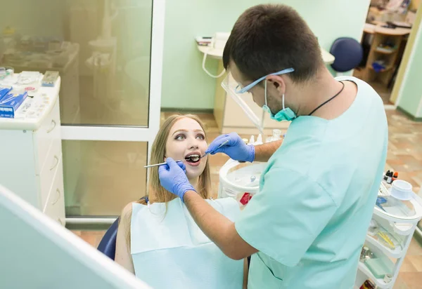 Close-up picture of young woman sitting in the dentists chair with opened mouth at dentists office while having examination — Stock Photo, Image