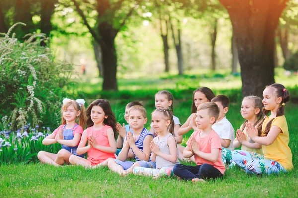 Un gran grupo de niños dedicados al yoga en el Parque sentados sobre la hierba —  Fotos de Stock