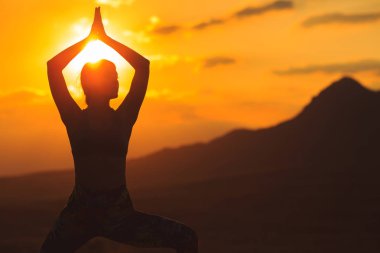 Güzel dağ yerinde gün batımında veya gün doğumunda yoga veya pilates yapan genç kadının silueti