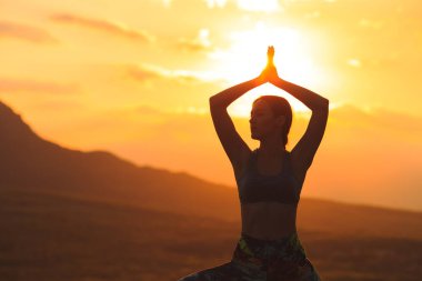 Güzel dağ yerinde gün batımında veya gün doğumunda yoga veya pilates yapan genç kadının silueti