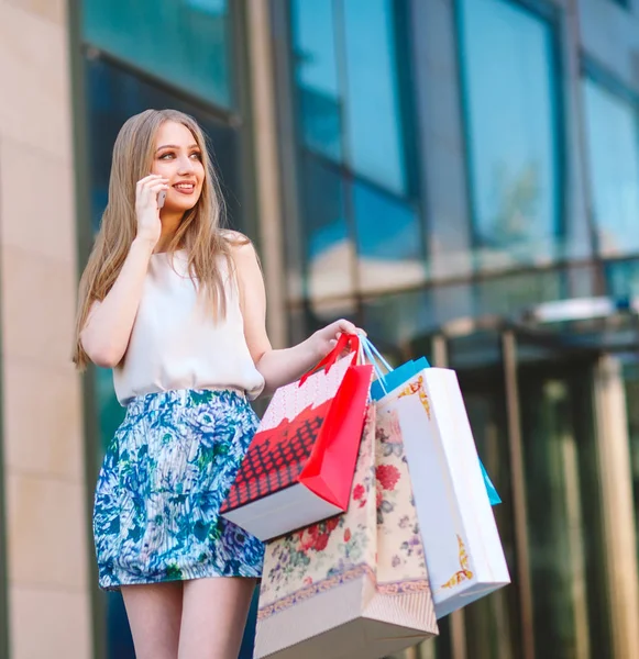 Lifestyleporträt junges blondes Mädchen, mit Einkaufstüten, die aus dem Geschäft gehen und mit dem Handy sprechen — Stockfoto