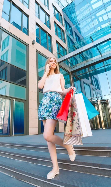 라이프 스타일 초상화 젊은 금발 소녀, 쇼핑 백에서 밖으로 걸어 와서 휴대 전화로 이야기. — 스톡 사진