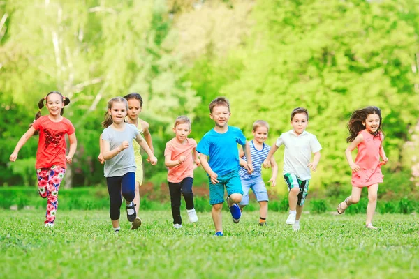 Viele verschiedene Kinder, Jungen und Mädchen, die an sonnigen Sommertagen in Freizeitkleidung durch den Park laufen — Stockfoto