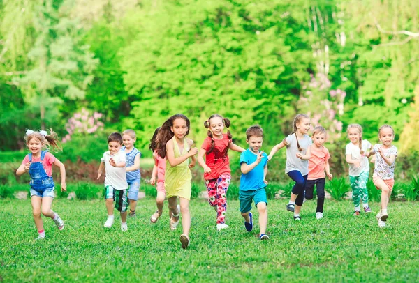 Molti bambini, ragazzi e ragazze diversi che corrono nel parco nella soleggiata giornata estiva in abiti casual . — Foto Stock