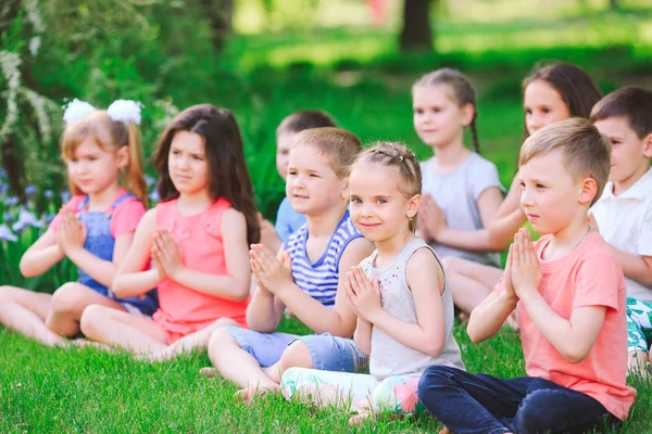 Un gran grupo de niños dedicados al yoga en el Parque sentados sobre la hierba —  Fotos de Stock