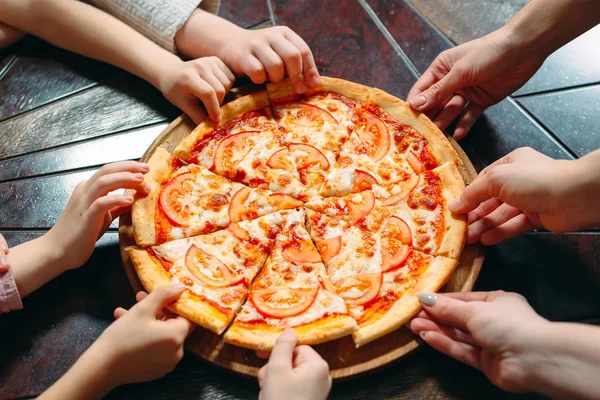 Hands taking pizza slices from wooden table, close up view. — Stock Photo, Image