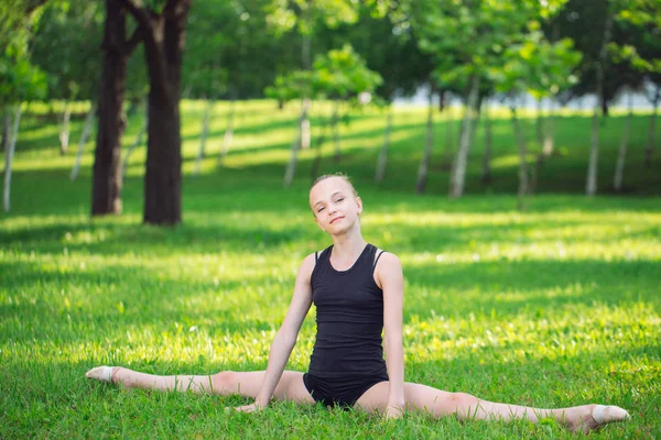 Vacker liten flicka gör gymnastik på gräset på en solig dag — Stockfoto