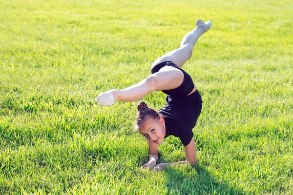 Beautiful little girl doing gymnastics on the grass on a sunny day. — Stock Photo, Image