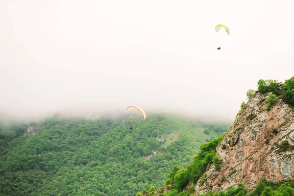 Yamaç paraşütçüleri ile güzel manzara. Bulutlu havalarda yeşil dağlar — Stok fotoğraf