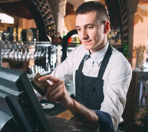 Малый бизнес, люди и концепция обслуживания - счастливый человек или официант в фартуке за стойкой с кассой, работающей в баре или кафе. — стоковое фото