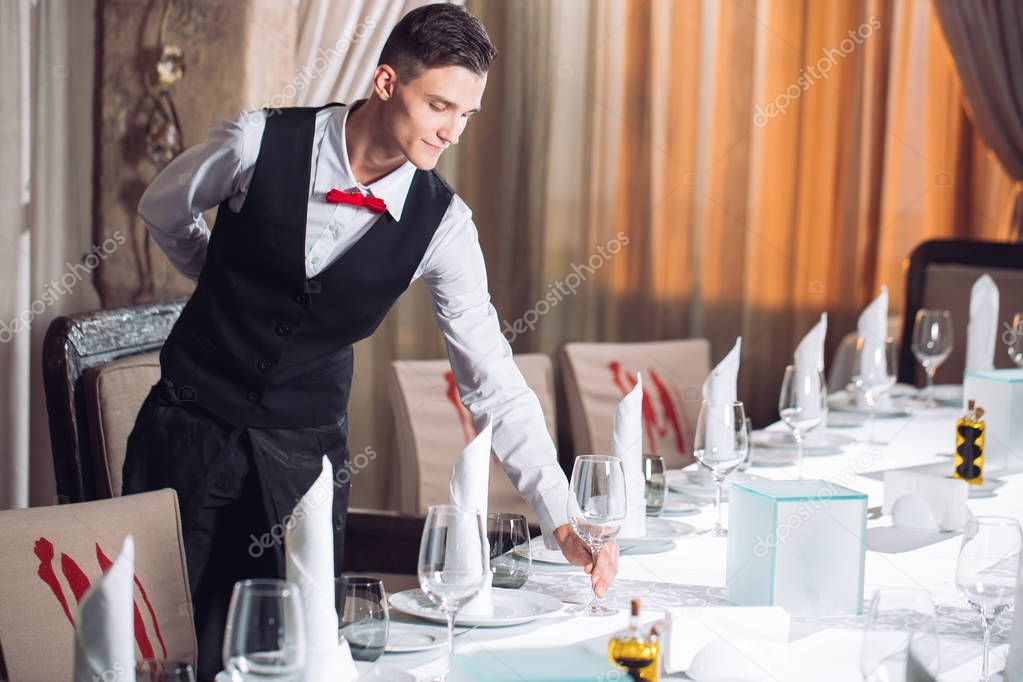 Waiter serving table in the restaurant preparing to receive guests.