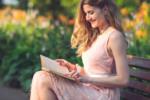 Een jong meisje het lezen van een boek zittend op een bankje bij zonsondergang — Stockfoto