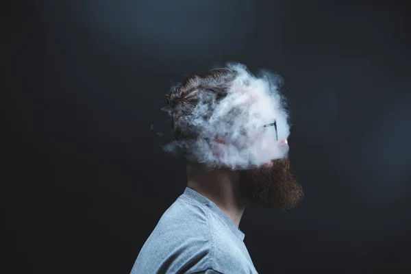 Konzept. Rauch umhüllte den Kopf des Mannes. Porträt eines bärtigen, stylischen Mannes mit Rauch. Passivrauchen. — Stockfoto