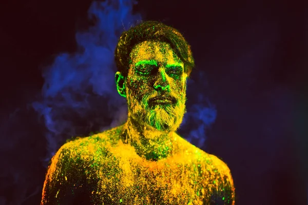 Hombre barbudo pintado en polvo fluorescente sobre un fondo de humo —  Fotos de Stock