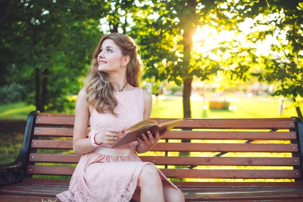 Een jong meisje het lezen van een boek zittend op een bankje bij zonsondergang — Stockfoto