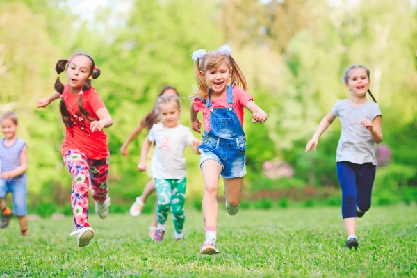 Molti bambini, ragazzi e ragazze diversi che corrono nel parco nella soleggiata giornata estiva in abiti casual — Foto Stock