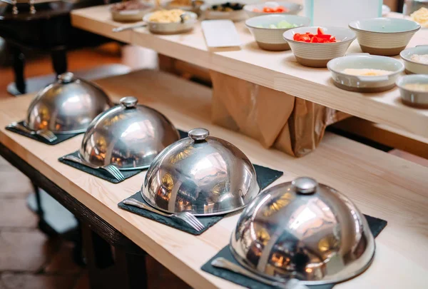 Buffet in een restaurant of hotel. Metalen schotels met dop. — Stockfoto