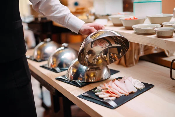 Разрезание мяса на тарелке. Официант держит металлическую крышку от плиты открытой. — стоковое фото