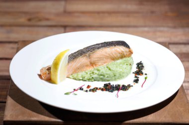 Ahşap bir masanın arka planında beyaz bir tabak üzerinde limon ile Balık biftek.