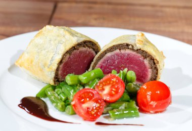 Ahşap bir masanın arka planında beyaz bir tabak üzerinde brokoli püresi ile domuz bonfile.