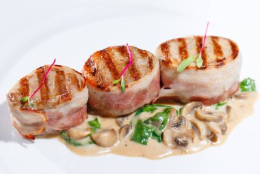 Ahşap bir masanın arka planında beyaz bir tabak üzerinde mantar soslu kızarmış et.