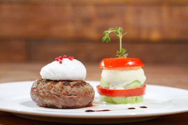 Ahşap bir masanın arka planında beyaz bir tabakta et ve yumurta ile yemek.