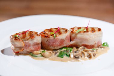 Ahşap bir masanın arka planında beyaz bir tabak üzerinde mantar soslu kızarmış et.