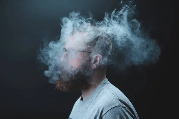 Konzept. Rauch umhüllte den Kopf des Mannes. Porträt eines bärtigen, stylischen Mannes mit Rauch. Passivrauchen — Stockfoto