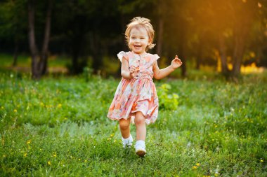 Parkta çim üzerinde çalışan mutlu sevimli küçük kız. Mutluluk.