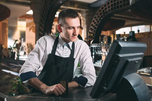 Малый бизнес, люди и концепция обслуживания - счастливый человек или официант в фартуке за стойкой с кассой, работающей в баре или кафе — стоковое фото