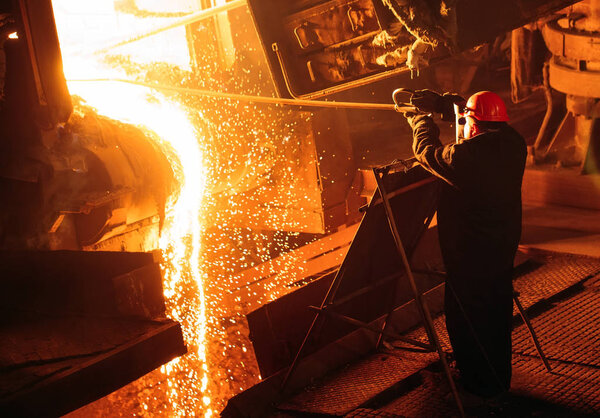 Plant for the production of steel. An electric melting furnace. Factory worker takes a sample for metal.