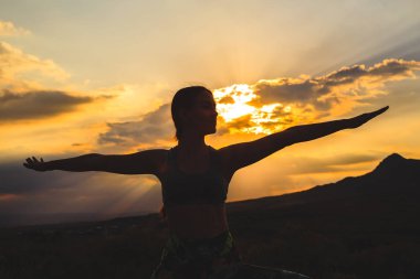 Güzel dağ yerinde gün batımında veya gün doğumunda yoga veya pilates yapan genç kadının silueti.