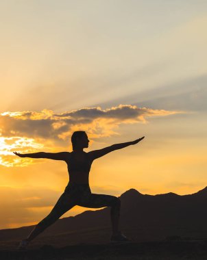 Güzel dağ yerinde gün batımında veya gün doğumunda yoga veya pilates yapan genç kadının silueti.