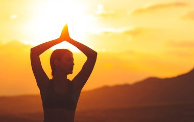 Güzel dağ yerinde gün batımında veya gün doğumunda yoga veya pilates yapan genç kadının silueti.