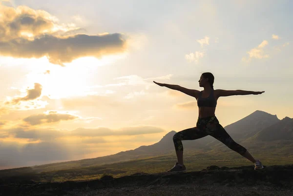 Silueta de mujer joven practicando yoga o pilates al atardecer o al amanecer en una hermosa ubicación de montaña . — Foto de Stock