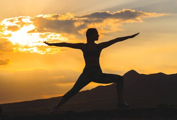 Silueta de mujer joven practicando yoga o pilates al atardecer o al amanecer en una hermosa ubicación de montaña . — Foto de Stock