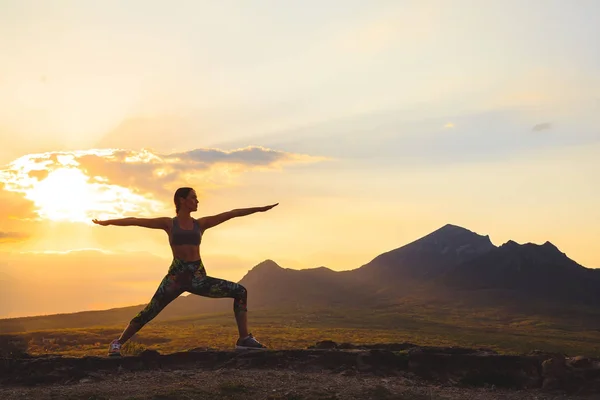 Silueta de mujer joven practicando yoga o pilates al atardecer o al amanecer en una hermosa ubicación de montaña . — Foto de Stock