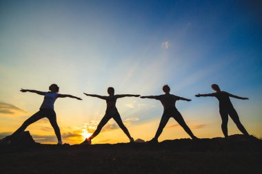 Güzel dağ yerinde gün batımında veya gün doğumunda yoga veya pilates yapan genç kadın silueti.