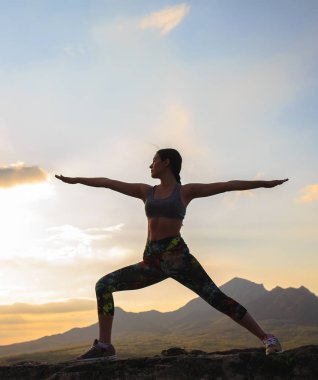 Güzel dağ yerinde gün batımında veya gün doğumunda yoga veya pilates yapan genç kadının silueti.