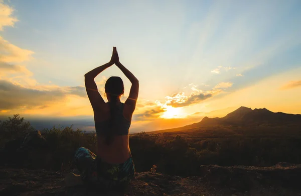 Mujer joven practicando yoga o pilates al atardecer o al amanecer en una hermosa ubicación de montaña . — Foto de Stock