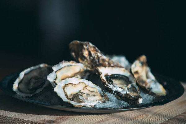 Oysters on the black plate on wooden background.