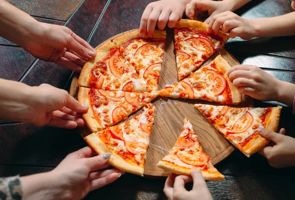 Mãos tirando fatias de pizza da mesa de madeira, vista de perto . — Fotografia de Stock