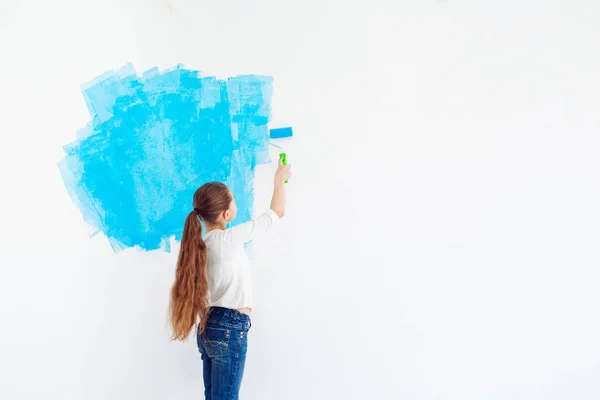 Reparación en el apartamento. Niña feliz pinta la pared con pintura azul, — Foto de Stock