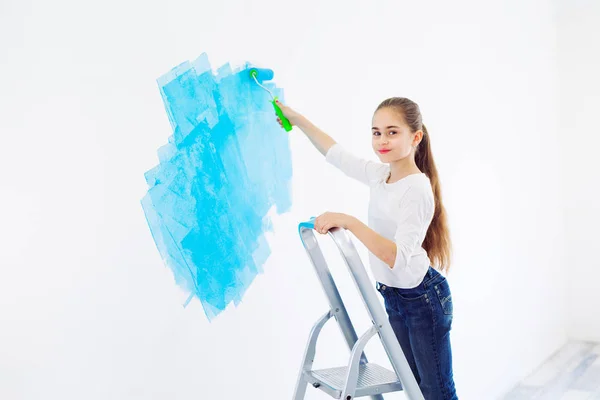 Reparación en el apartamento. Niña feliz pinta la pared con pintura azul, — Foto de Stock