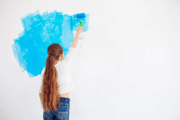 Reparación en el apartamento. Niña feliz pinta la pared con pintura azul, — Foto de Stock