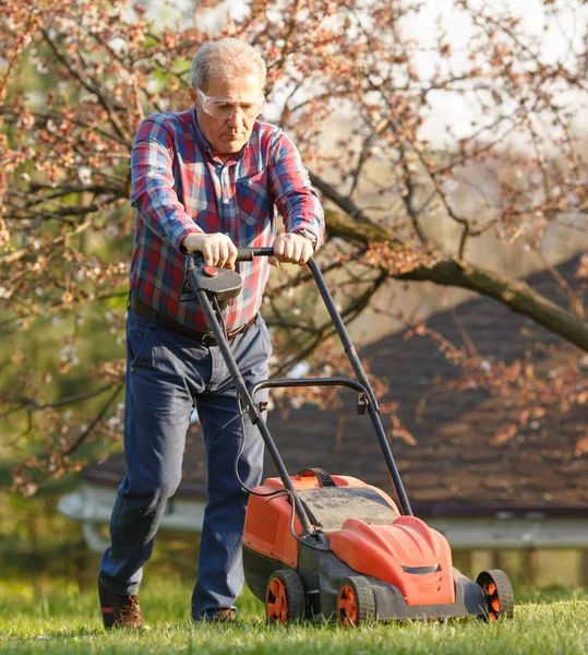Mann mit elektrischem Rasenmäher, Rasenmäher. Gärtner beim Trimmen eines Gartens. Sonniger Tag, Vorort, Dorf. — Stockfoto
